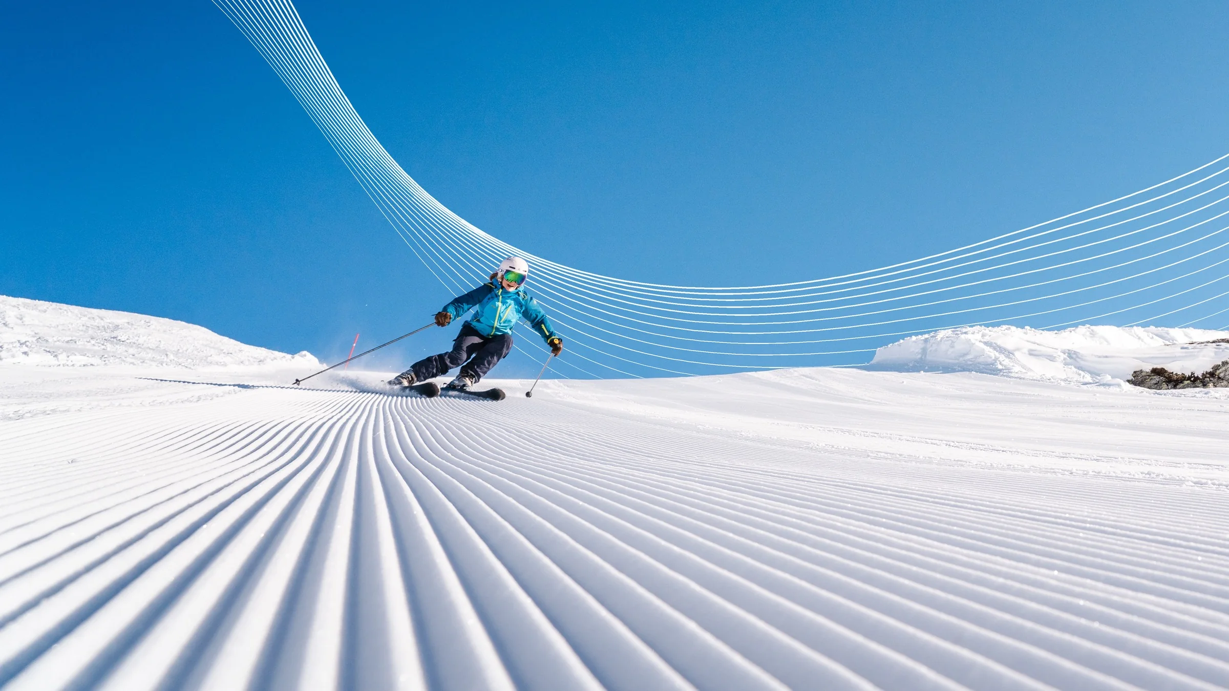 A skier in a teal jacket carves down a freshly groomed piste under a clear blue sky, with the white flowing lines of the Ski Solutions We Make It Yours campaign sweeping behind her.