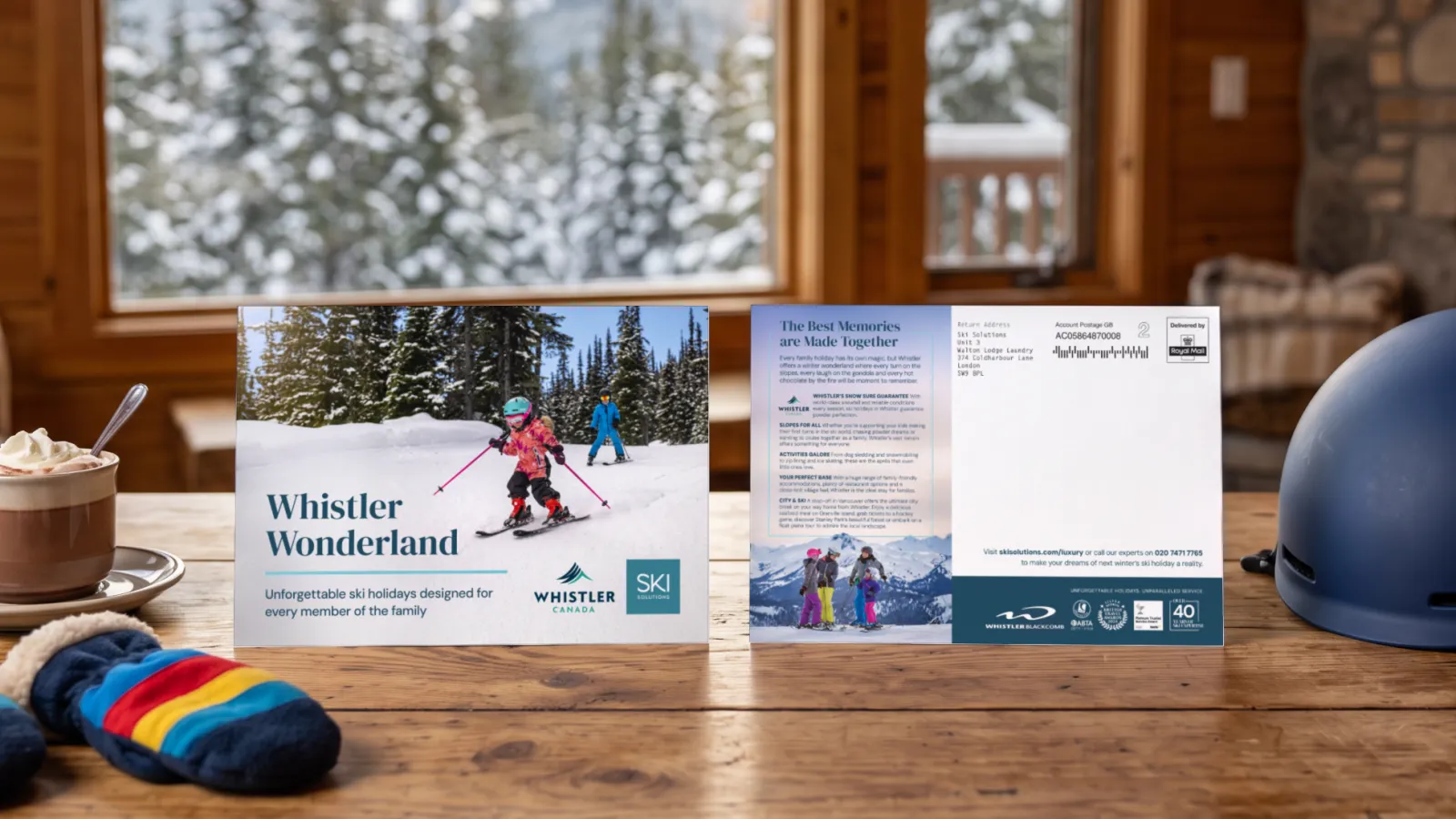 The Ski Solutions Whistler Wonderland mailer, front and back, standing on a family chalet table with hot chocolate and children’s ski mittens, in a portfolio visualisation.